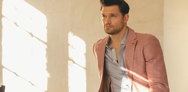 A man looking into the distance while wearing a blue shirt and pink jacket