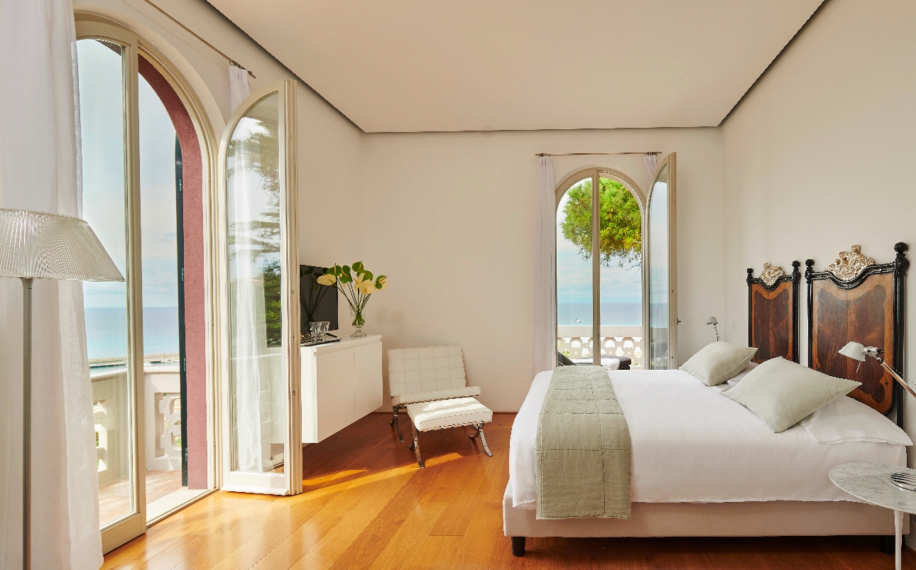 A bedroom with a large bed and windows looking out to the sea