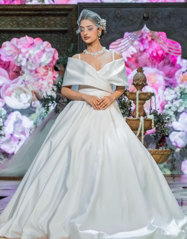 model in traditional princess gown on runway with cross over panels on bust and birdcage veil